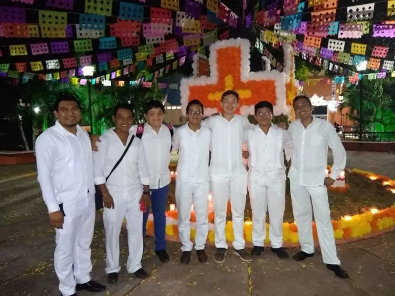 Siete integrantes de la orquesta frente a un altar con papel picado